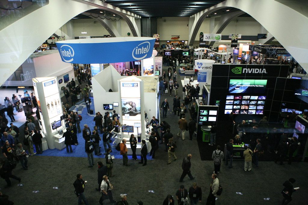 Overhead view of the GDC 2011 expo floor at Moscone Center, crowded with attendees between tall Intel and NVIDIA booths under white arched ceiling beams