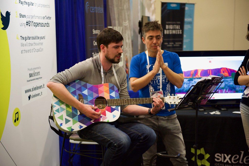 Two attendees play a custom guitar at the sixeleven booth during DrupalCon Nashville