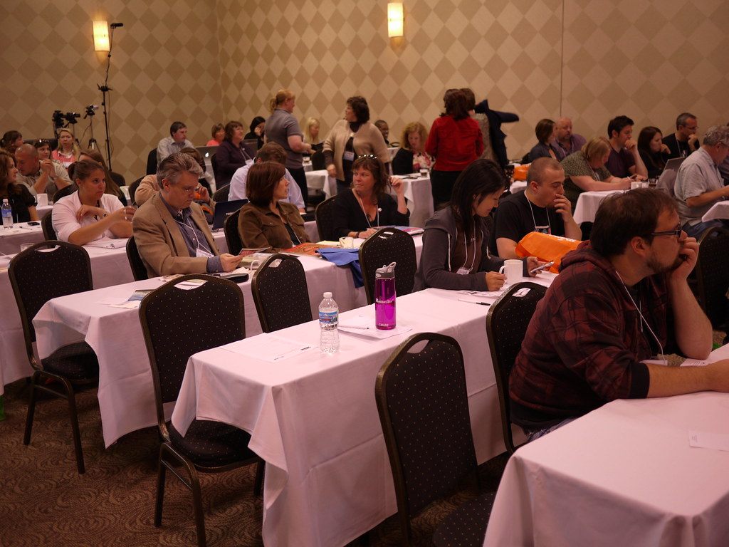 Attendees at white-draped classroom tables during a WordCamp Detroit 2010 session in a meeting room at the Novi hall, then the Rock Financial Showplace