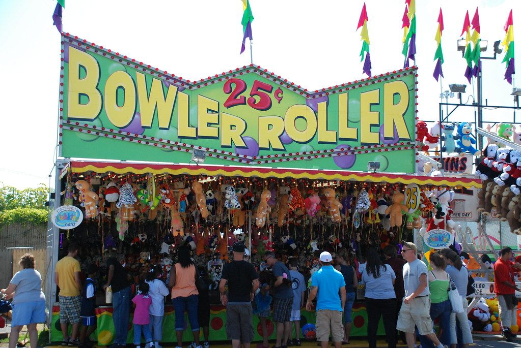 Fairgoers lined up at the Bowler Roller game booth, hung with stuffed-animal prizes, on the State Fair midway