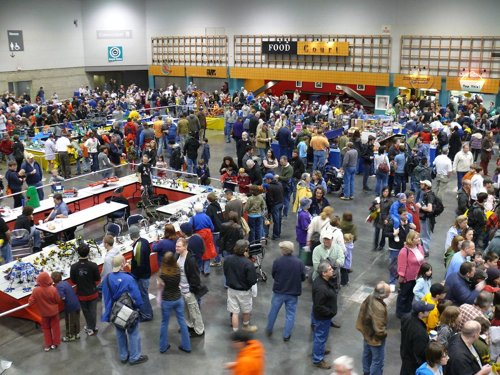 A dense crowd of families and fans moving between display tables in an Oregon Convention Center exhibit hall during BrickFest 2009