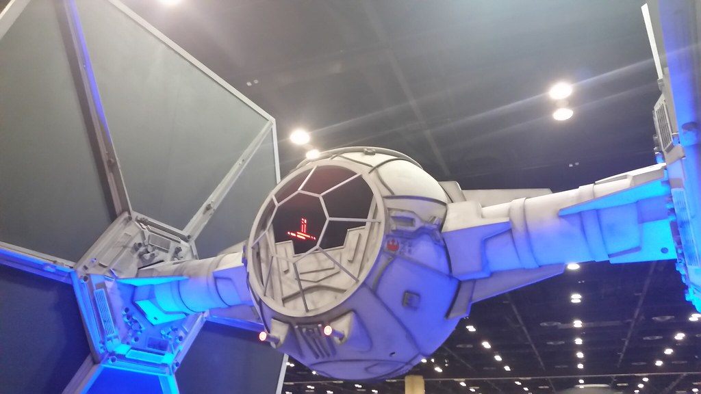A full-size TIE fighter replica lit in blue under the ceiling lights of an exhibit hall at Star Wars Celebration Orlando 2017