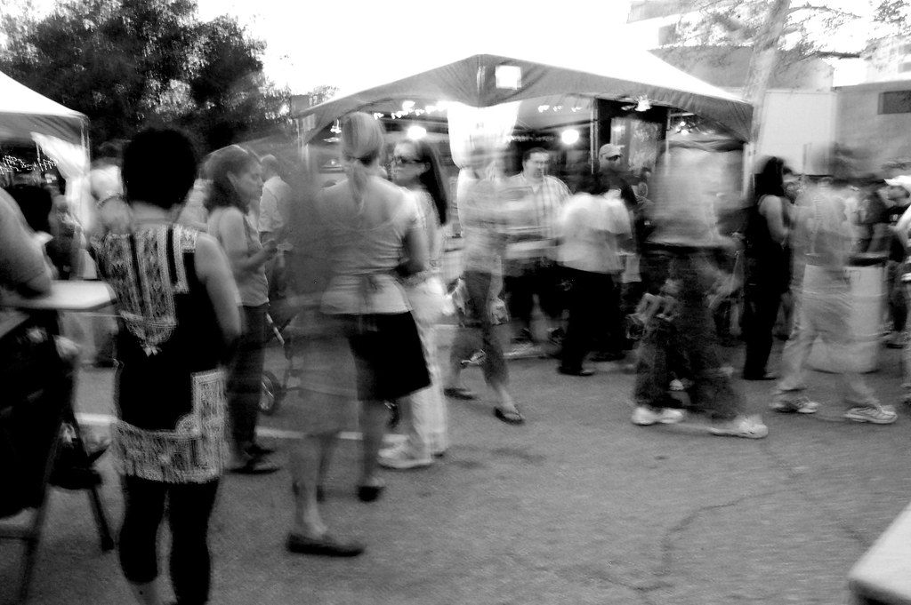A black-and-white long exposure of people moving between white festival tents at a downtown Oklahoma City arts festival