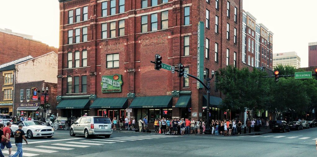 A crowd gathers on a street corner at Broadway in downtown Nashville on a summer evening