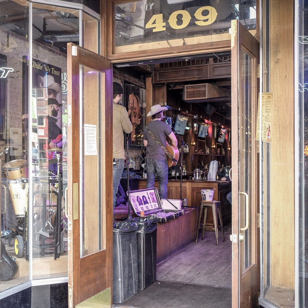A singer in a cowboy hat performs inside the open doors of a honky-tonk at 409 Broadway