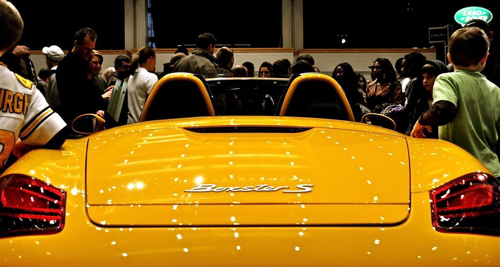 A crowd gathered around a yellow Porsche Boxster S at the 2011 Philadelphia Auto Show