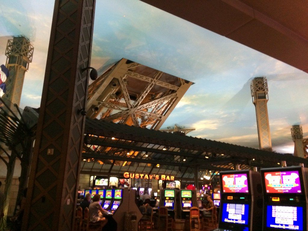 A steel leg of the Eiffel Tower replica coming down through the painted-sky ceiling over slot machines and a bar in the Paris casino