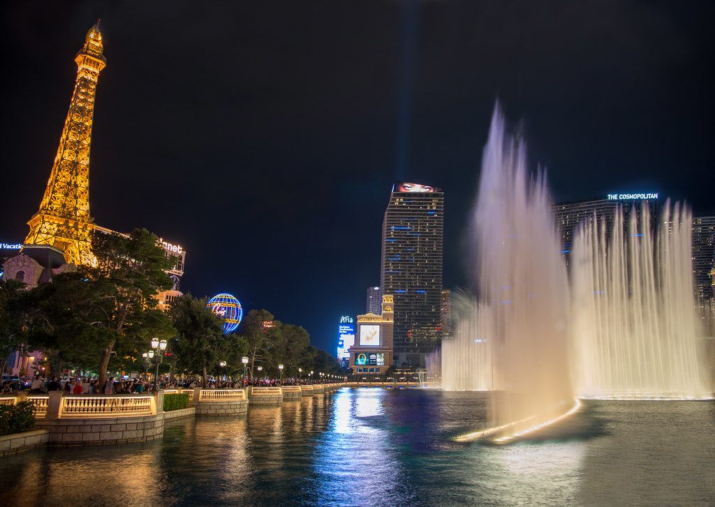 The lit Eiffel Tower replica and Paris balloon sign at night across the Bellagio fountains, with Strip towers behind