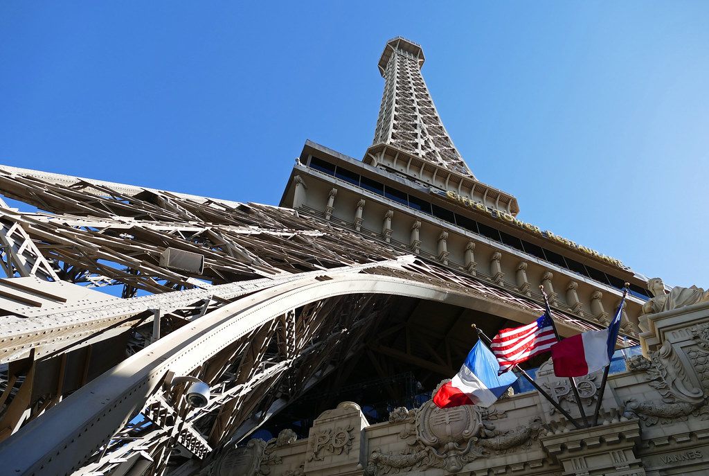 Looking up through the steel legs of the Eiffel Tower replica above the Paris Las Vegas façade, with French and U.S. flags