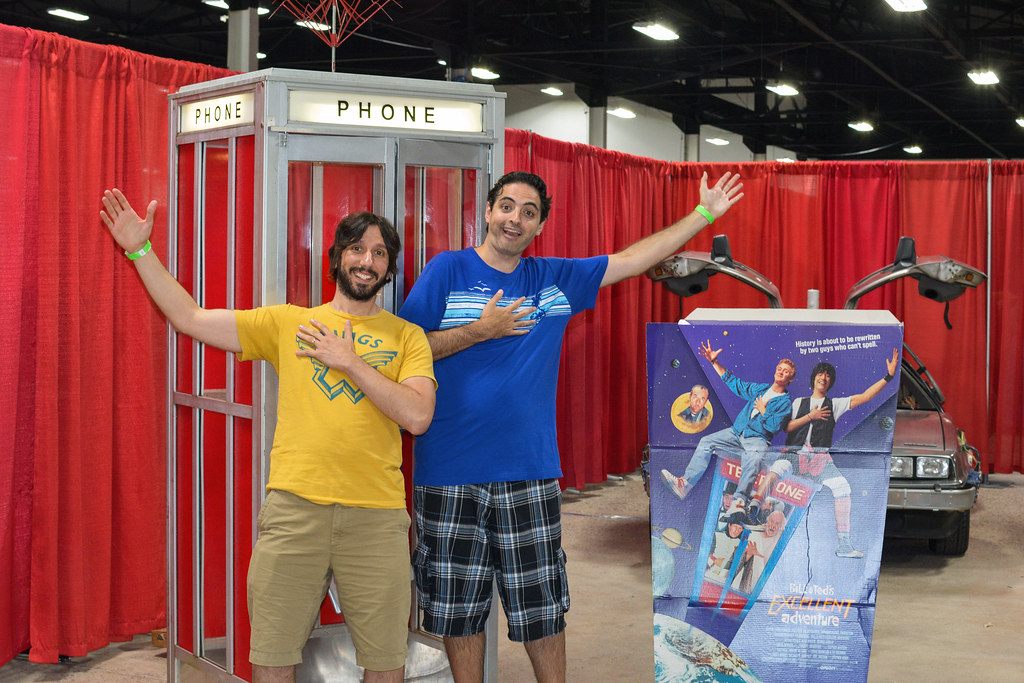 Two fans posing with arms spread beside a replica phone booth and a DeLorean at Retro Con in Oaks, PA