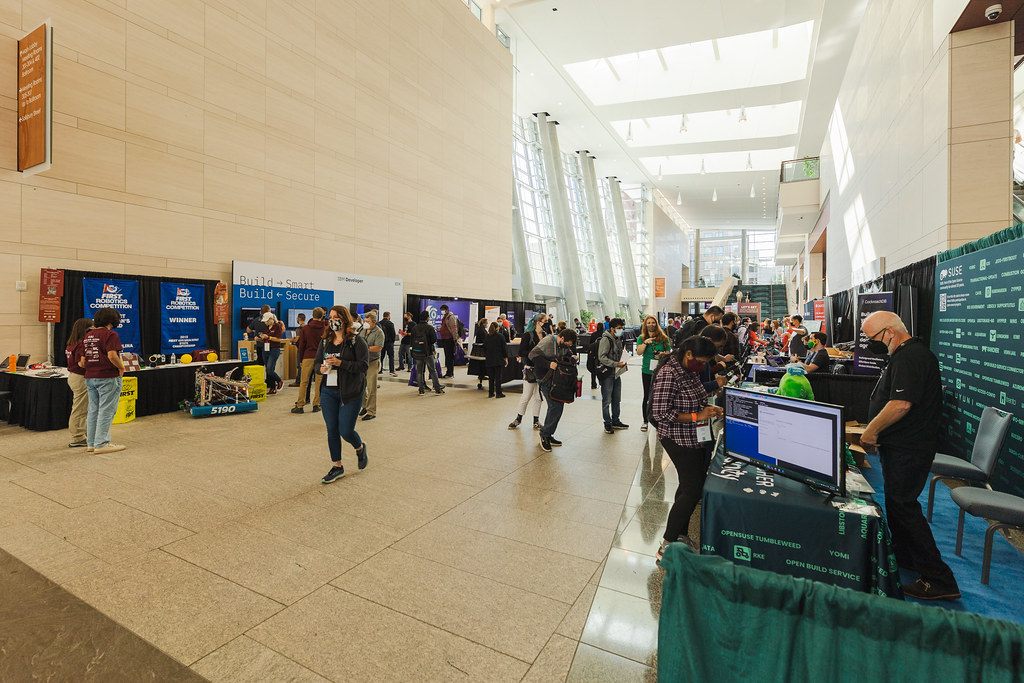Attendees browsing sponsor booths along the sunlit lobby of the Raleigh Convention Center at All Things Open 2021