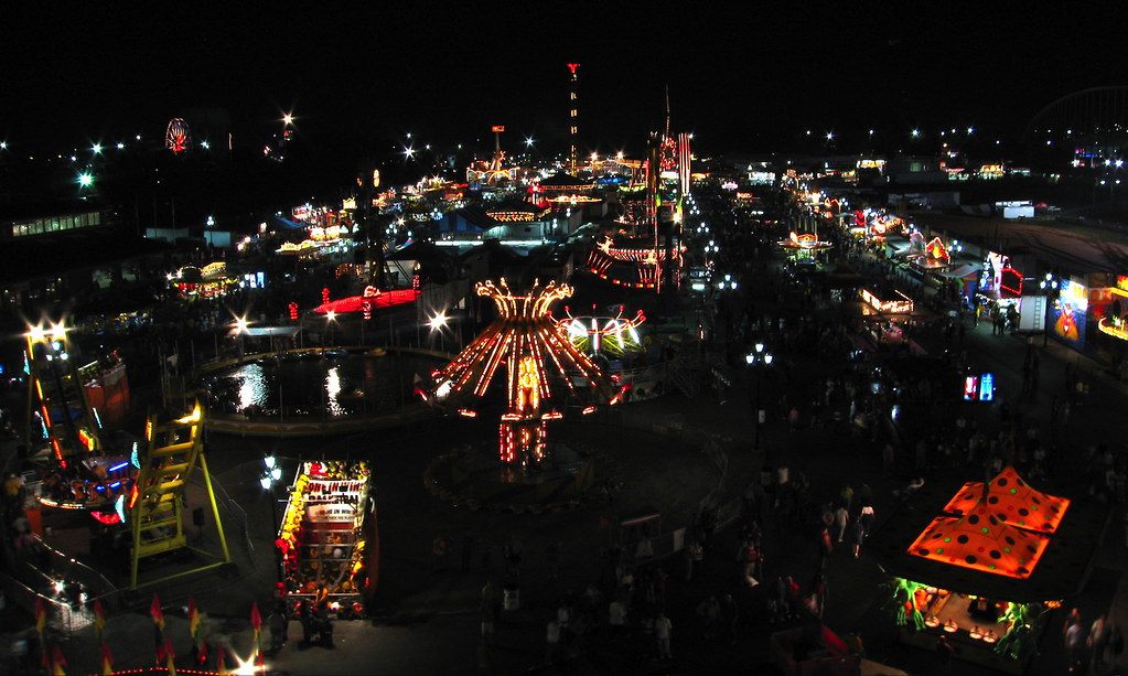 The lit-up midway of the N.C. State Fair at night seen from above, with rides, food stands and crowds along the paths