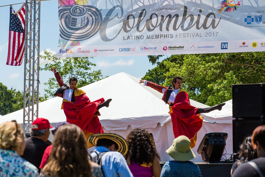 Dancers in flowing red skirts perform on an outdoor stage for a sunlit crowd at the Latino Memphis Festival 2017
