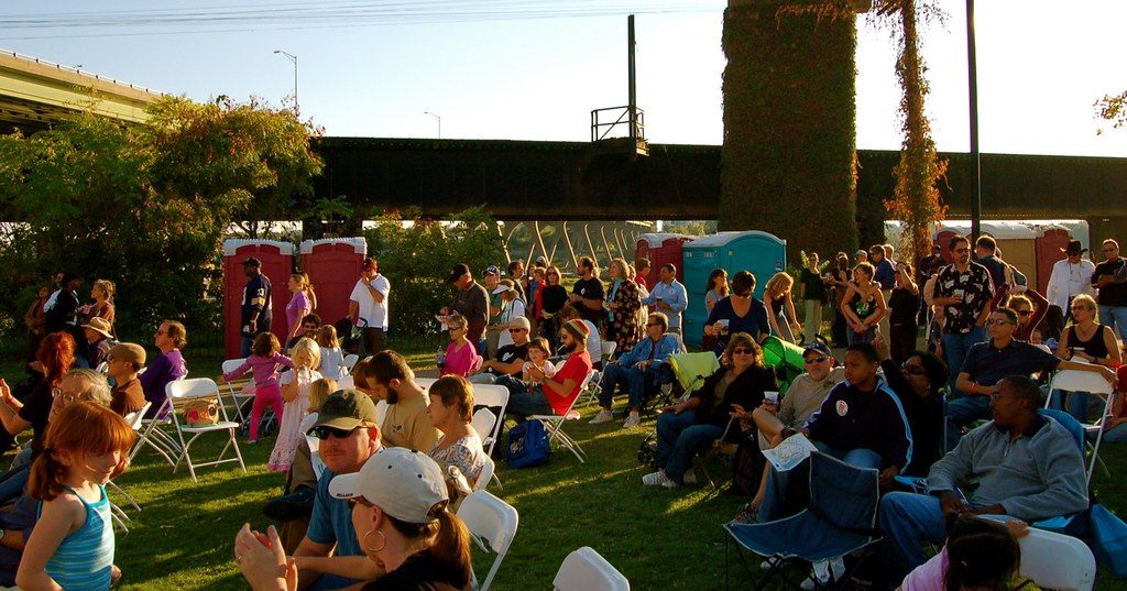 Families on lawn chairs and blankets at a late-afternoon festival on Brown's Island, under a railroad trestle by the James River