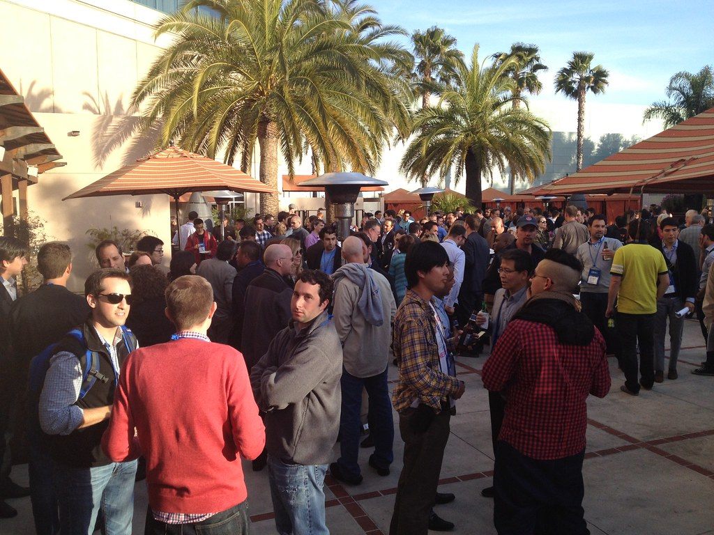 A crowd of DEMO Spring 2012 attendees mingling on a sunny palm-lined patio in Santa Clara
