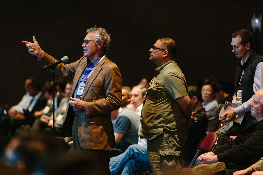 An attendee at a floor microphone asking a question during a session of the Linux Foundation's Open Networking Summit, with the audience seated around him
