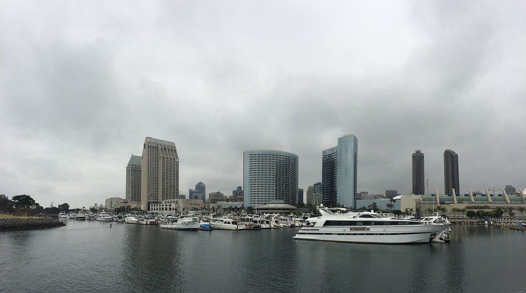 Downtown San Diego towers, including a round glass tower and a taller glass tower, rising behind a marina full of yachts on a gray day