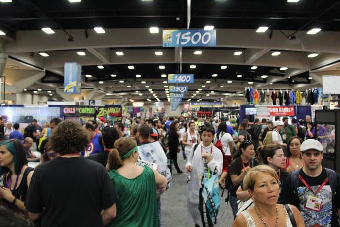 A packed aisle under numbered booth banners in the San Diego Convention Center exhibit hall during Comic-Con 2014