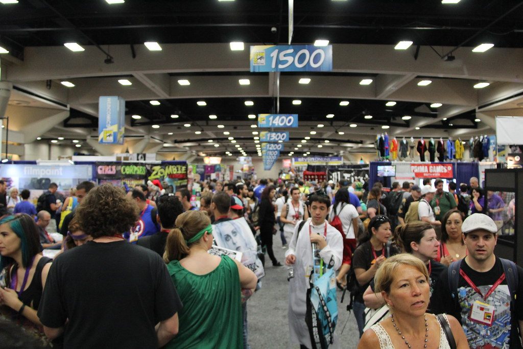 A packed aisle under numbered booth banners in the San Diego Convention Center exhibit hall during Comic-Con 2014