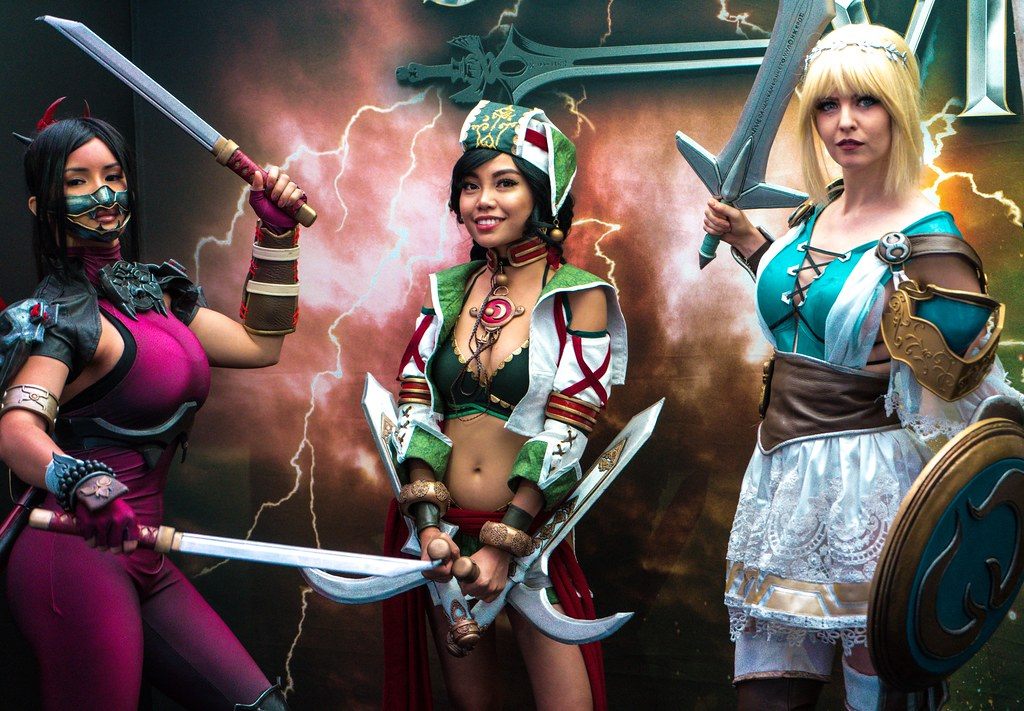 Three Soulcalibur cosplayers with swords posing in front of a stormy game backdrop at PAX West 2018
