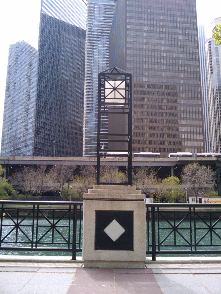 A lantern post on the riverside promenade with the Chicago River and downtown towers across the water