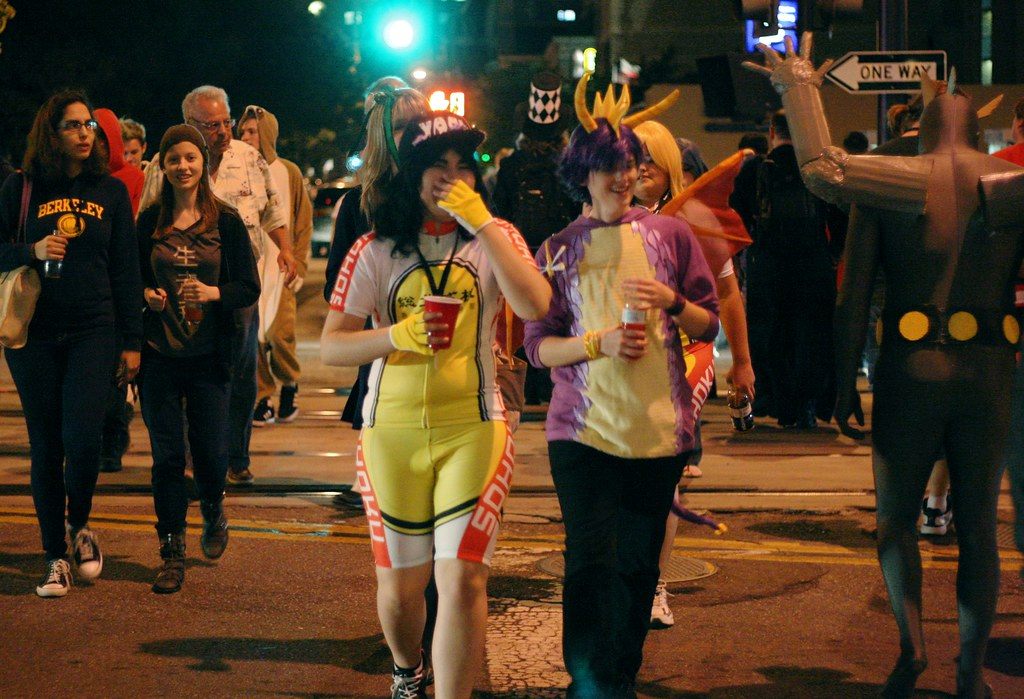 A crowd of costumed FanimeCon attendees crossing a downtown San Jose street at night
