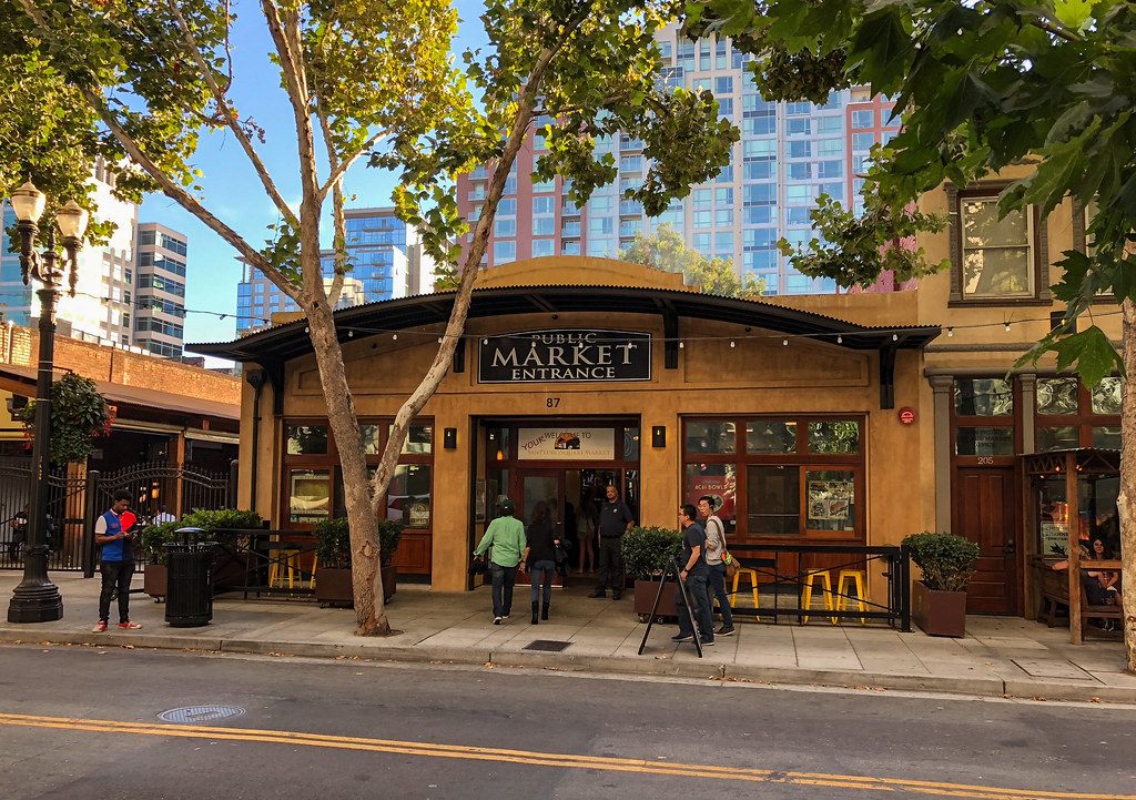 People walking past the Public Market entrance at San Pedro Square in downtown San Jose, under street trees