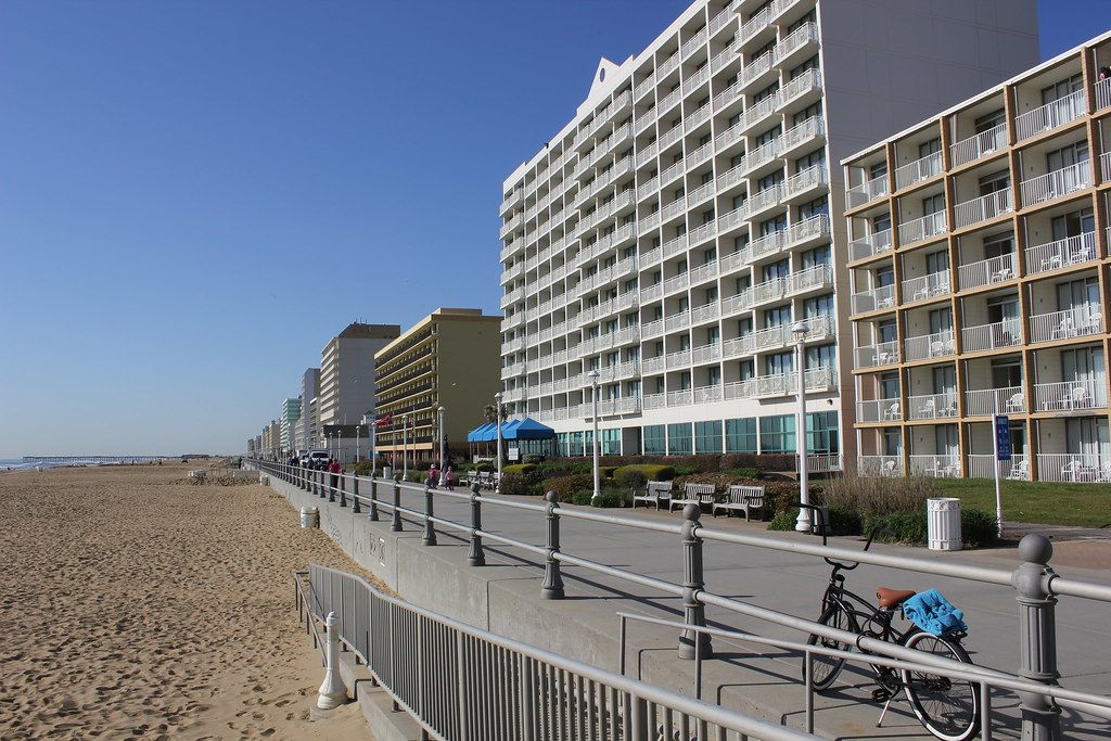 The Virginia Beach boardwalk and bike path running between the sand and a row of oceanfront hotels on a clear day