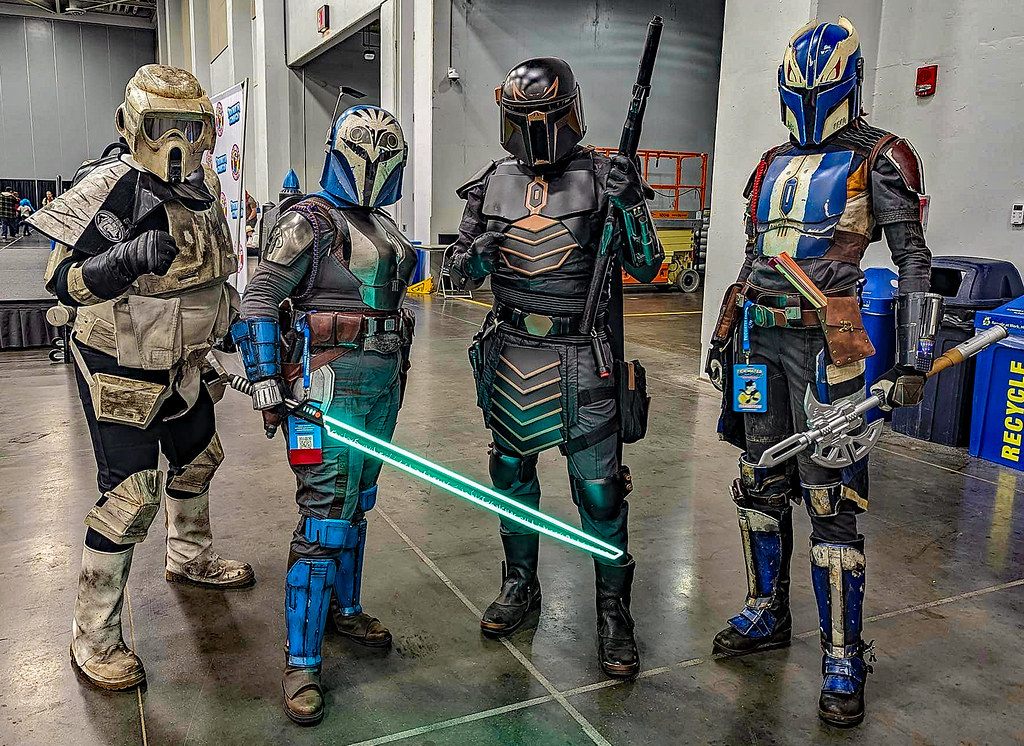 Four Star Wars cosplayers in Mandalorian and scout-trooper armor on the sealed concrete floor of a Virginia Beach Convention Center exhibit hall at Tidewater Comicon 2024