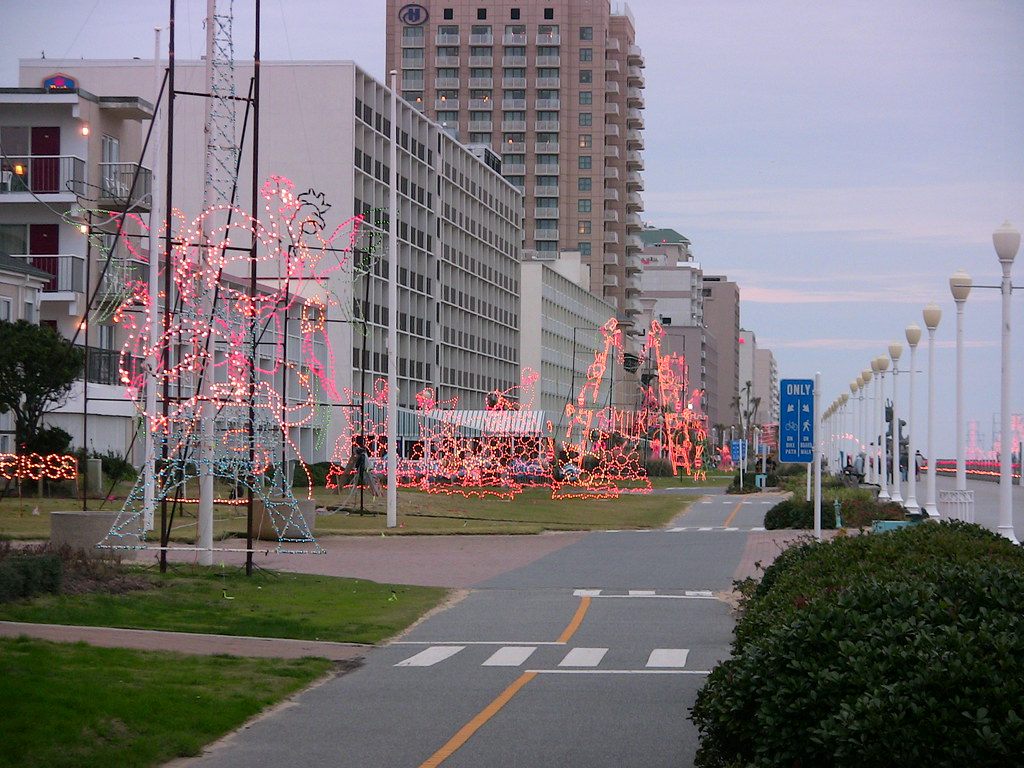 Pink and white holiday light sculptures lining the Virginia Beach boardwalk at dusk, with oceanfront hotels behind