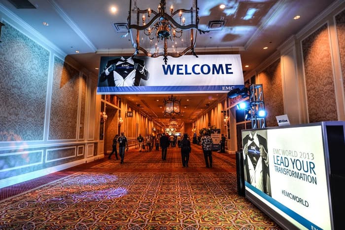 Attendees walking under a WELCOME banner and chandeliers down a carpeted convention corridor at the Venetian during EMC World 2013