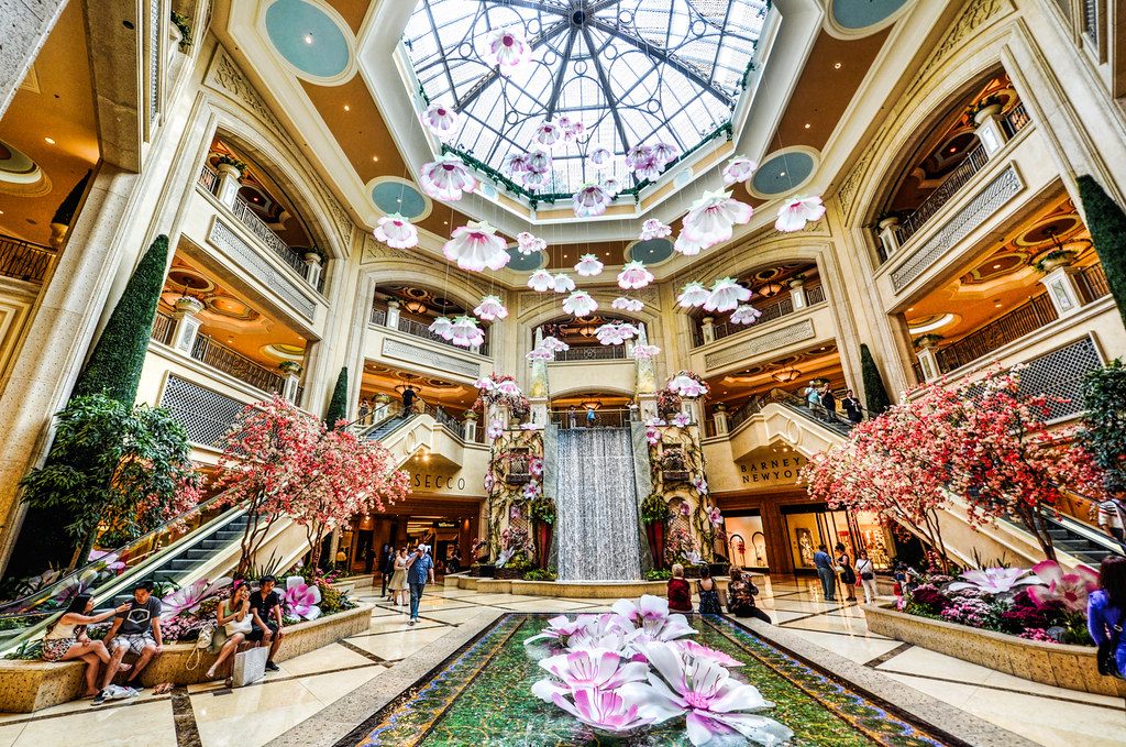 Visitors under the glass dome of the Palazzo waterfall atrium, decorated with giant hanging flowers and blossom trees