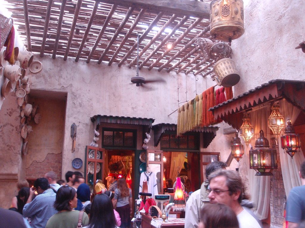 Visitors browse a crowded Moroccan-style market lane hung with lanterns and textiles in Epcot's World Showcase