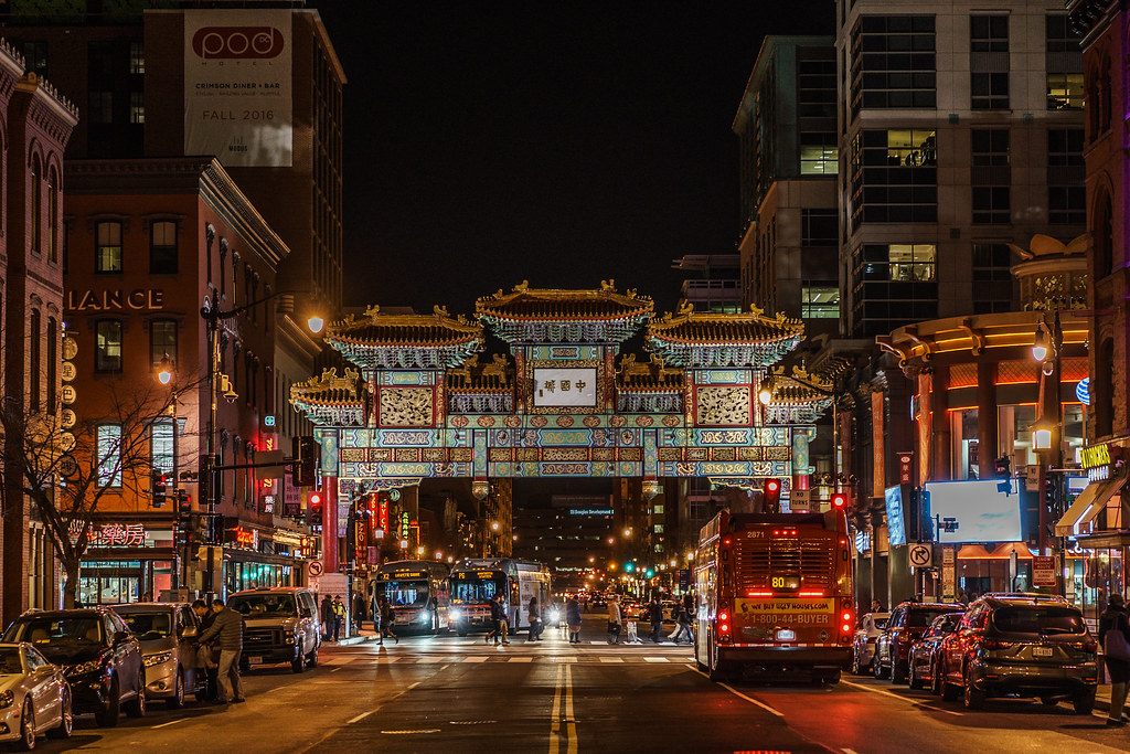 The lit Friendship Archway over H Street in Chinatown at night, with buses, restaurants and pedestrians