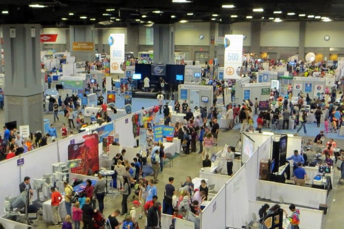 A busy exhibit floor in Hall A of the Walter E. Washington Convention Center, crowded with visitors among white-walled booths and tall banners