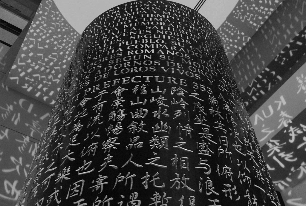 Black-and-white view of Lingua by Jim Sanborn, a tall cylinder covered in cut-out letters and characters from many languages