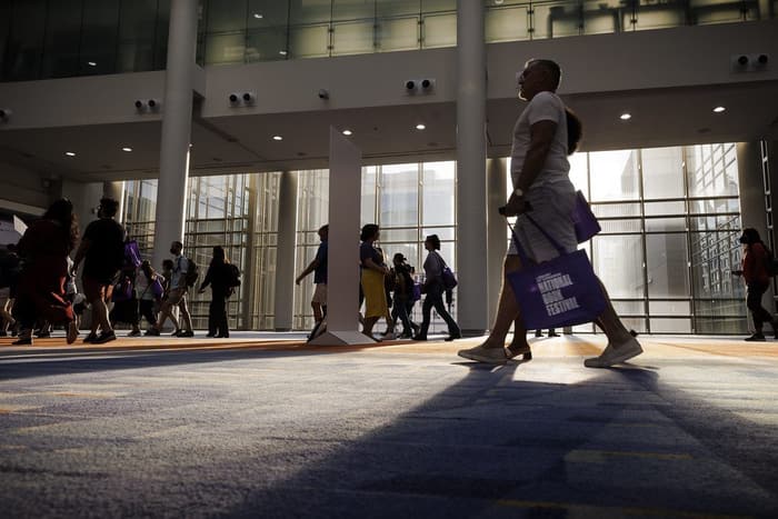 Silhouetted festival-goers carrying tote bags cross the sunlit glass lobby of the convention center during the National Book Festival