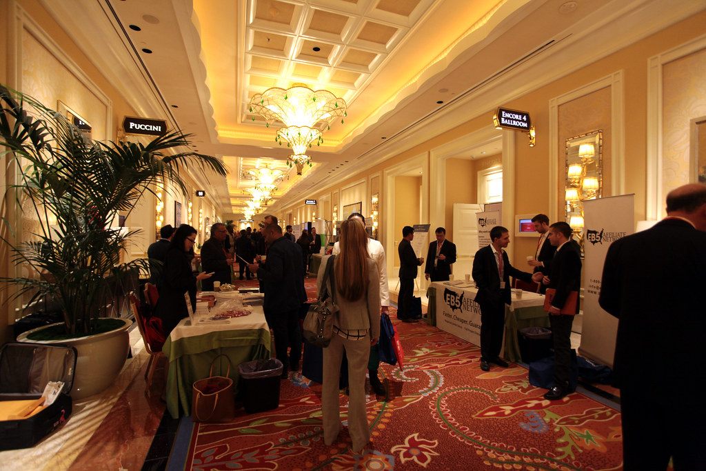 Attendees and tabletop exhibitors in the chandeliered foyer outside Encore Ballroom 4 during an EB-5 investor conference