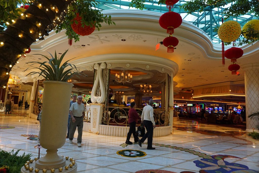 Guests walking across the mosaic floor of the Wynn Las Vegas main lobby under red lanterns and a glass atrium