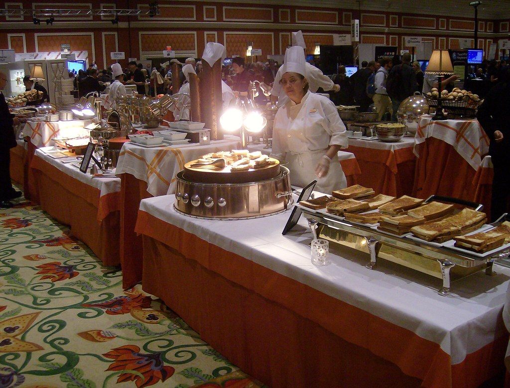 Chefs serving at catering stations while CES attendees crowd tech exhibitor tables at the ShowStoppers media event at the Wynn