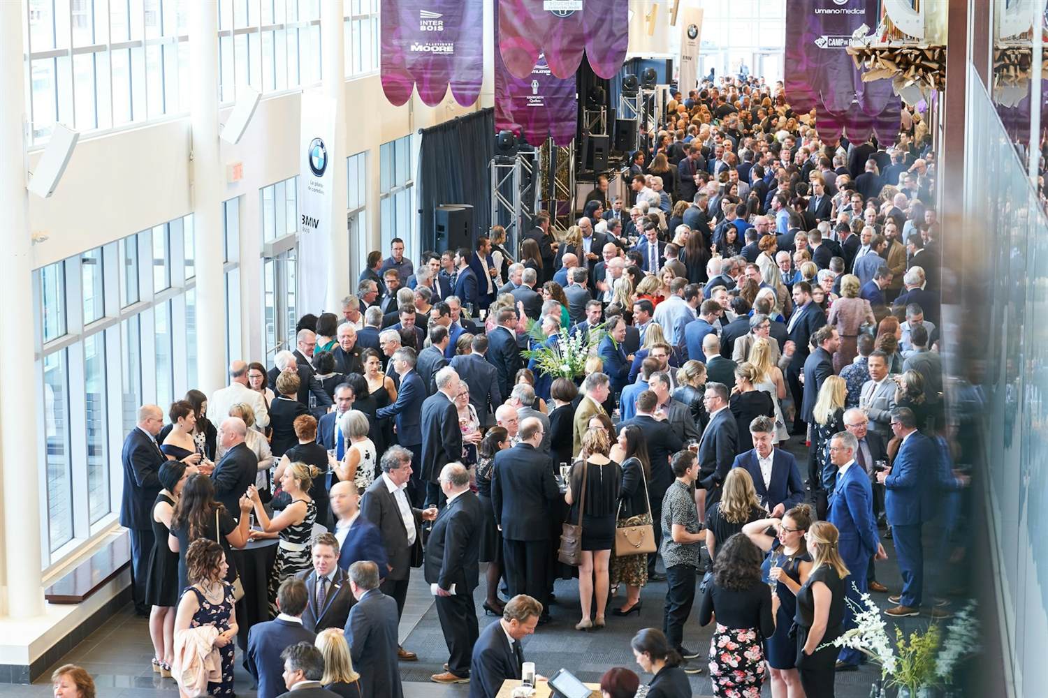 A packed opening reception in a convention center lobby with sponsor banners overhead