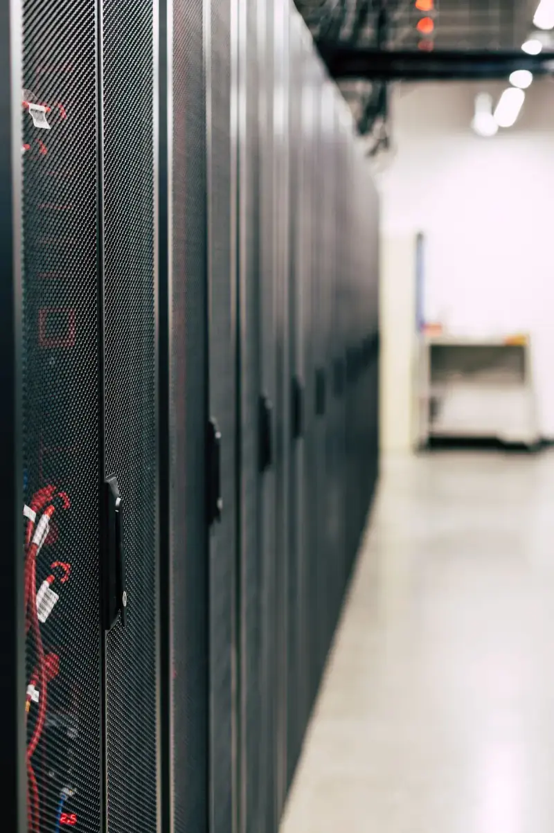 Row of tall black server cabinets with red cabling along a bright data hall aisle