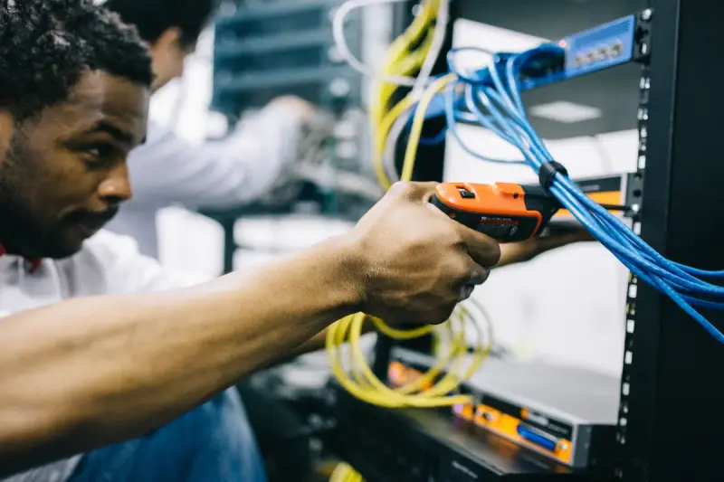 Engineer using a power screwdriver on rack equipment with yellow and blue cables