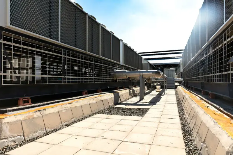 Rows of large industrial cooling units with metal grilles along a paved service walkway