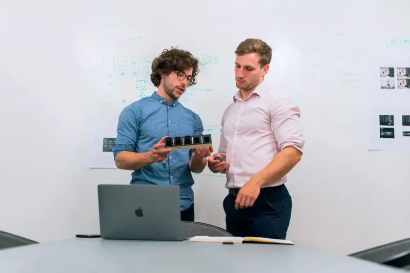 Two engineers in an office discuss a technology prototype on the table