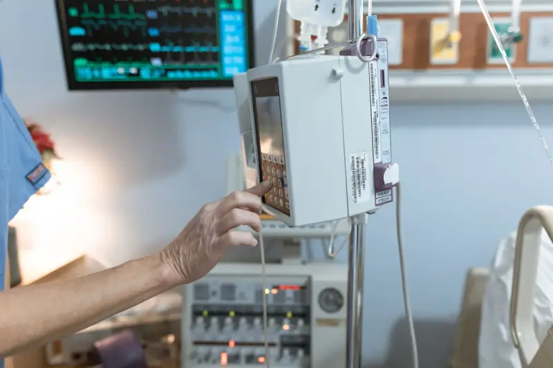 Gloved healthcare worker setting a modern infusion pump in a hospital room