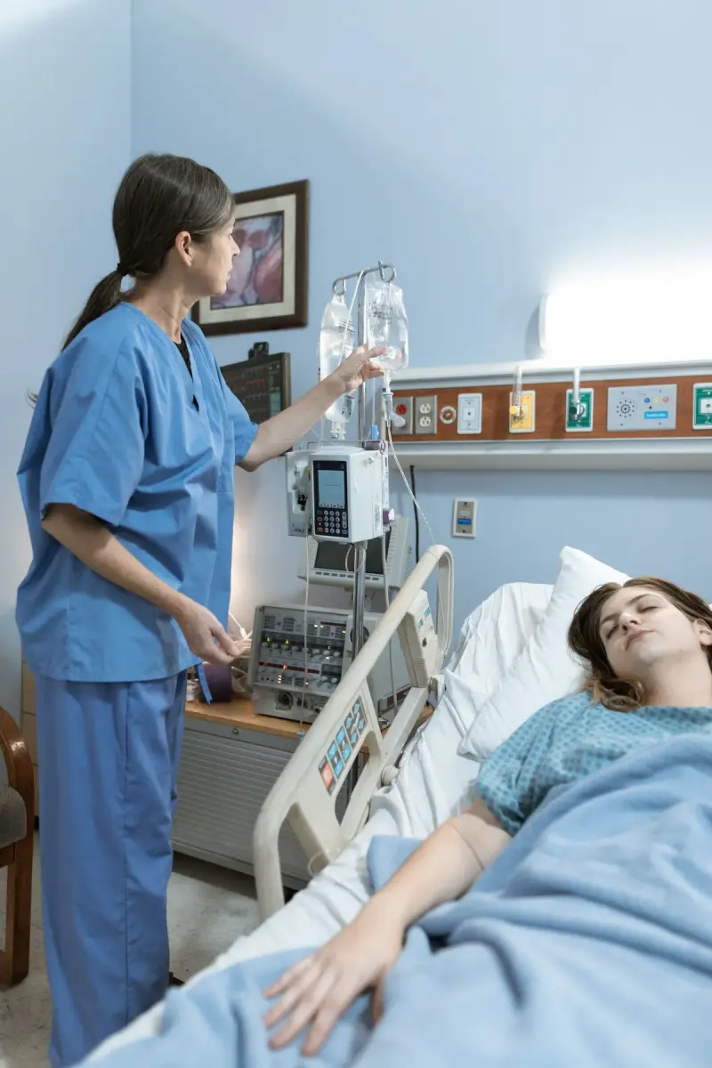 Nurse checking an IV line and equipment beside a patient in a hospital bed