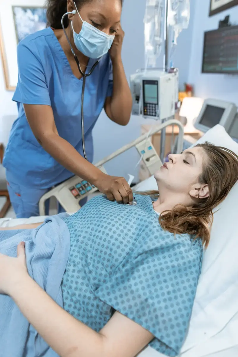 Nurse using a stethoscope on a woman lying in a hospital bed