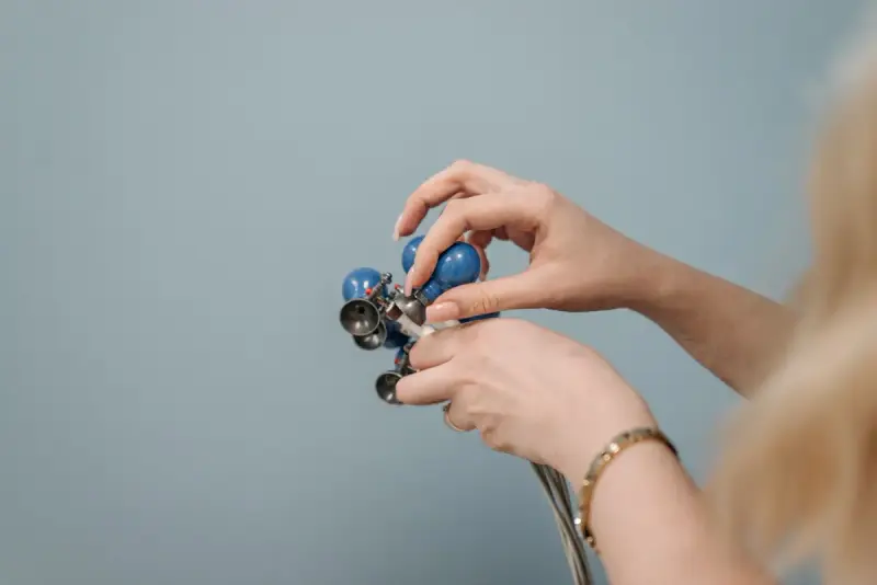 Hands sorting a bundle of blue suction electrodes on cables against a grey wall