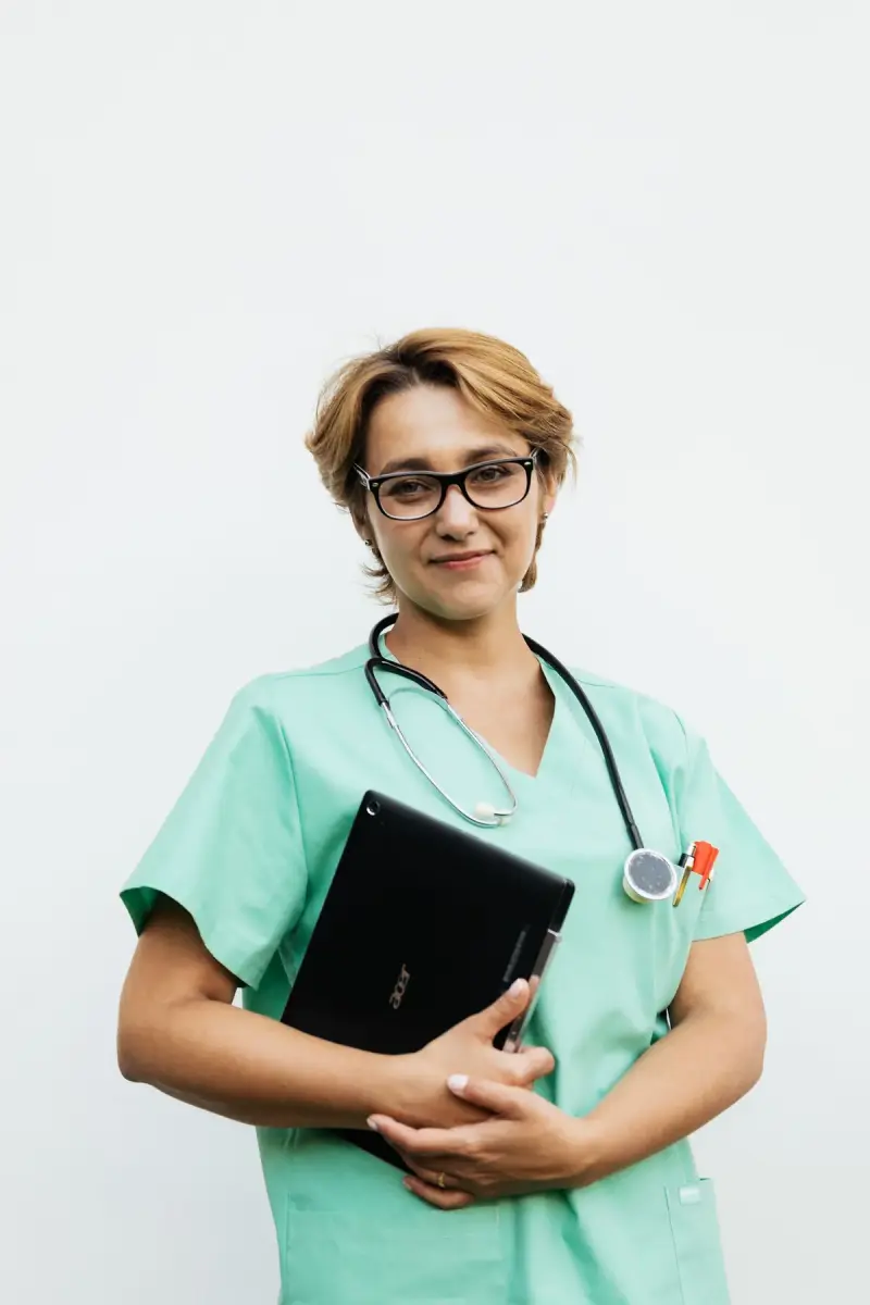 Woman in scrubs and eyeglasses holding a tablet with a stethoscope around her neck